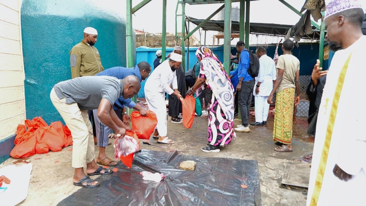 Members packing meat into red sacks on a black sheet in an open courtyard with blue walls.